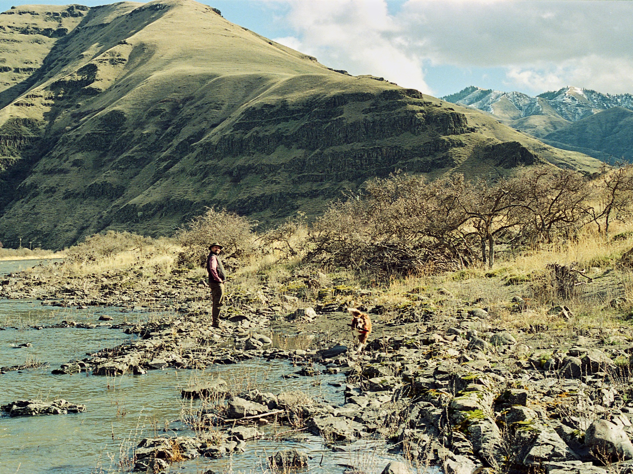 A man and dog moving through a rocky river canyon