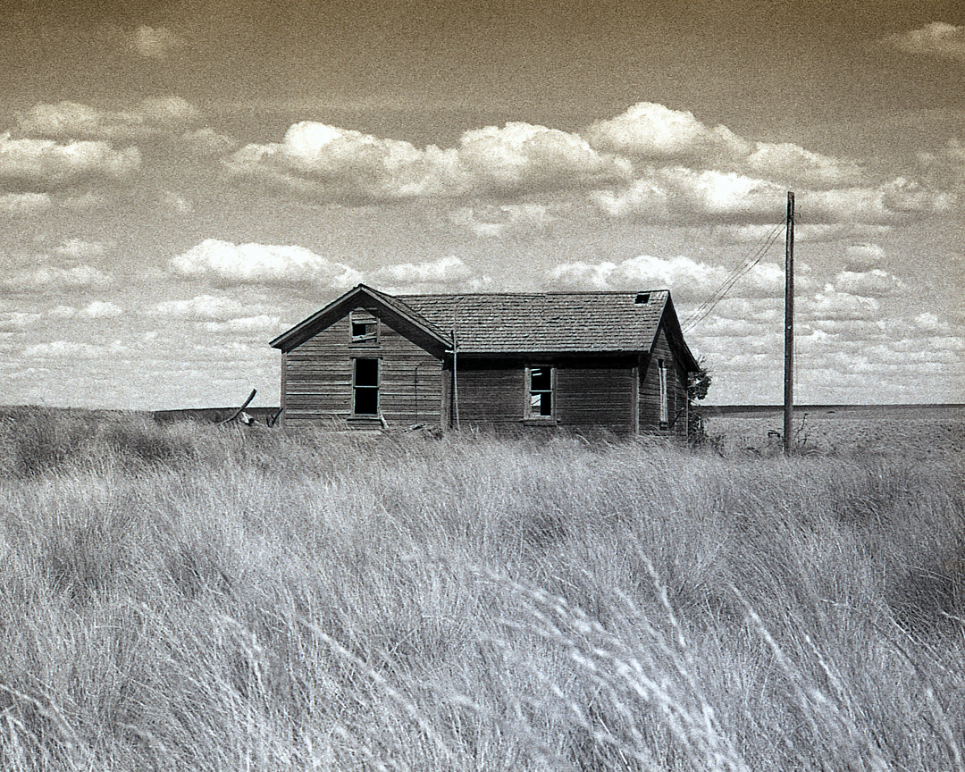 Abandoned wooden house in a field beneath clouds
