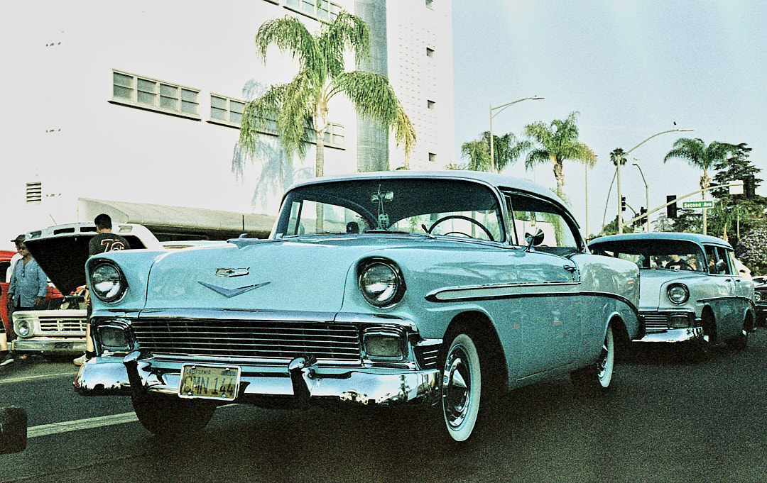 A pale blue classic Chevrolet on a palm lined street