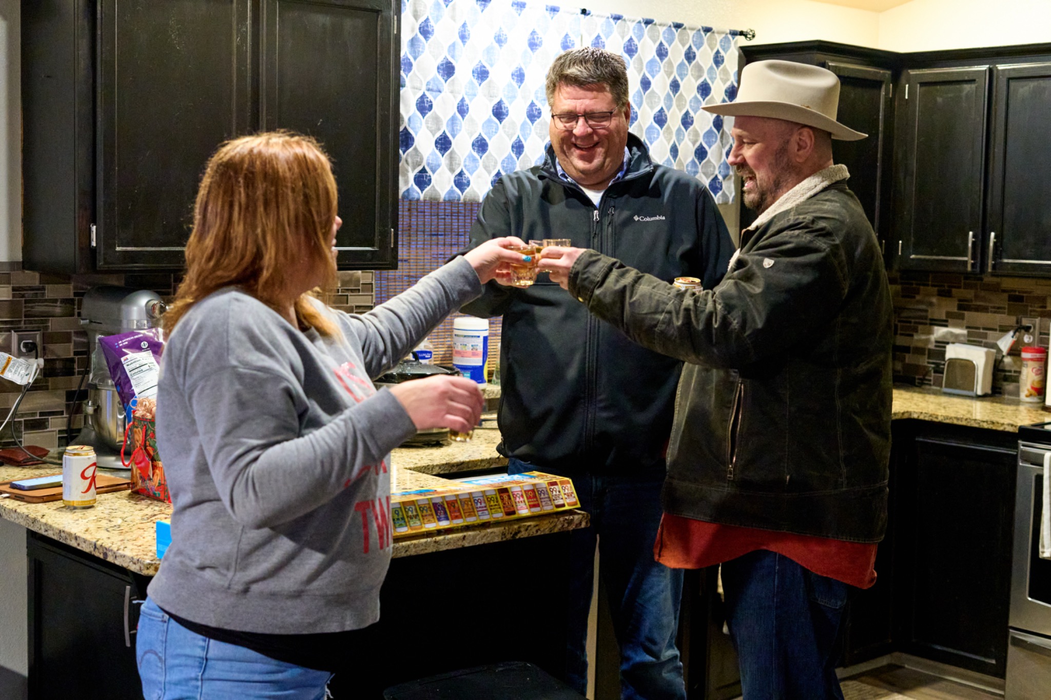 Three friends laughing and clinking glasses in the kitchen