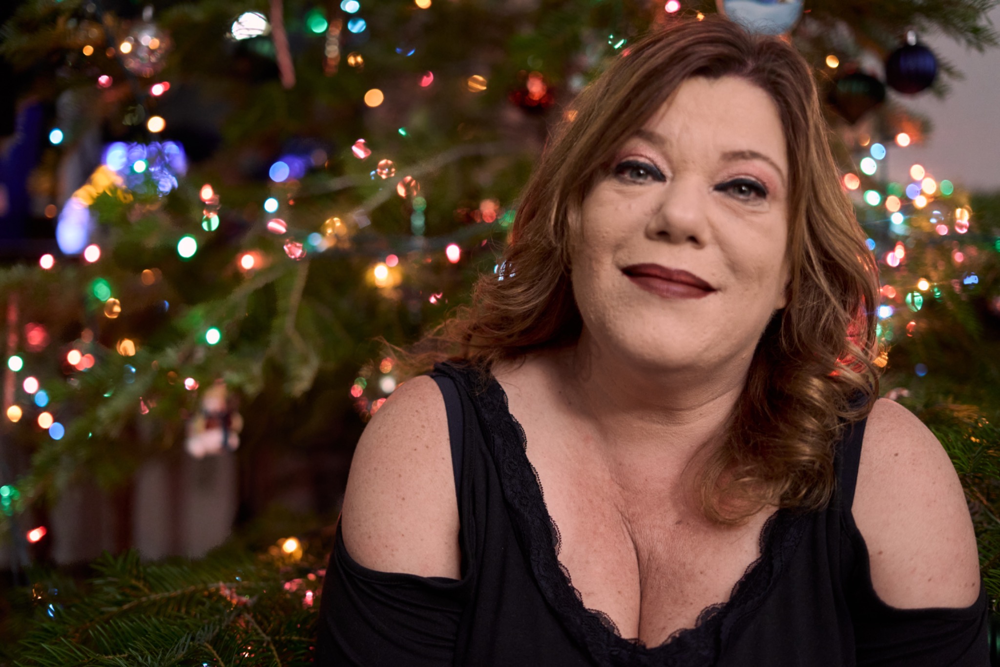 A woman smiling in front of a Christmas tree